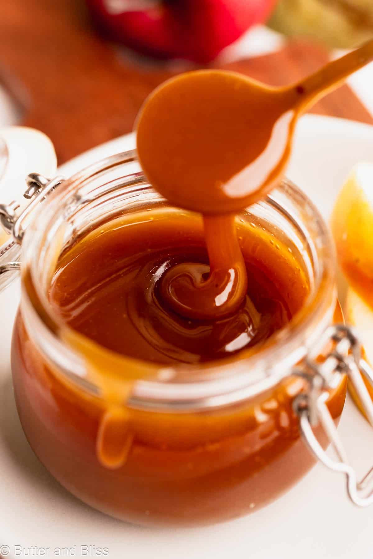 A ribbon of apple cider maple syrup caramel sauce dripping into a jar.