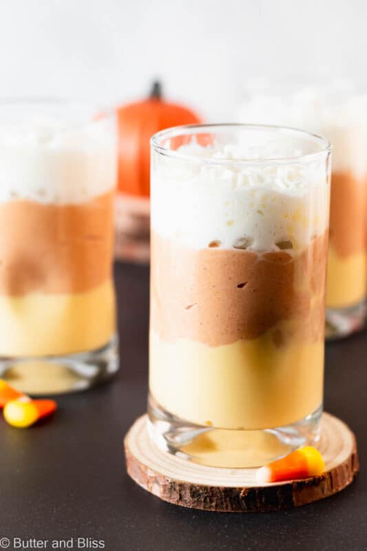 Creamy candy corn pudding in pretty parfait glasses on wood coasters.