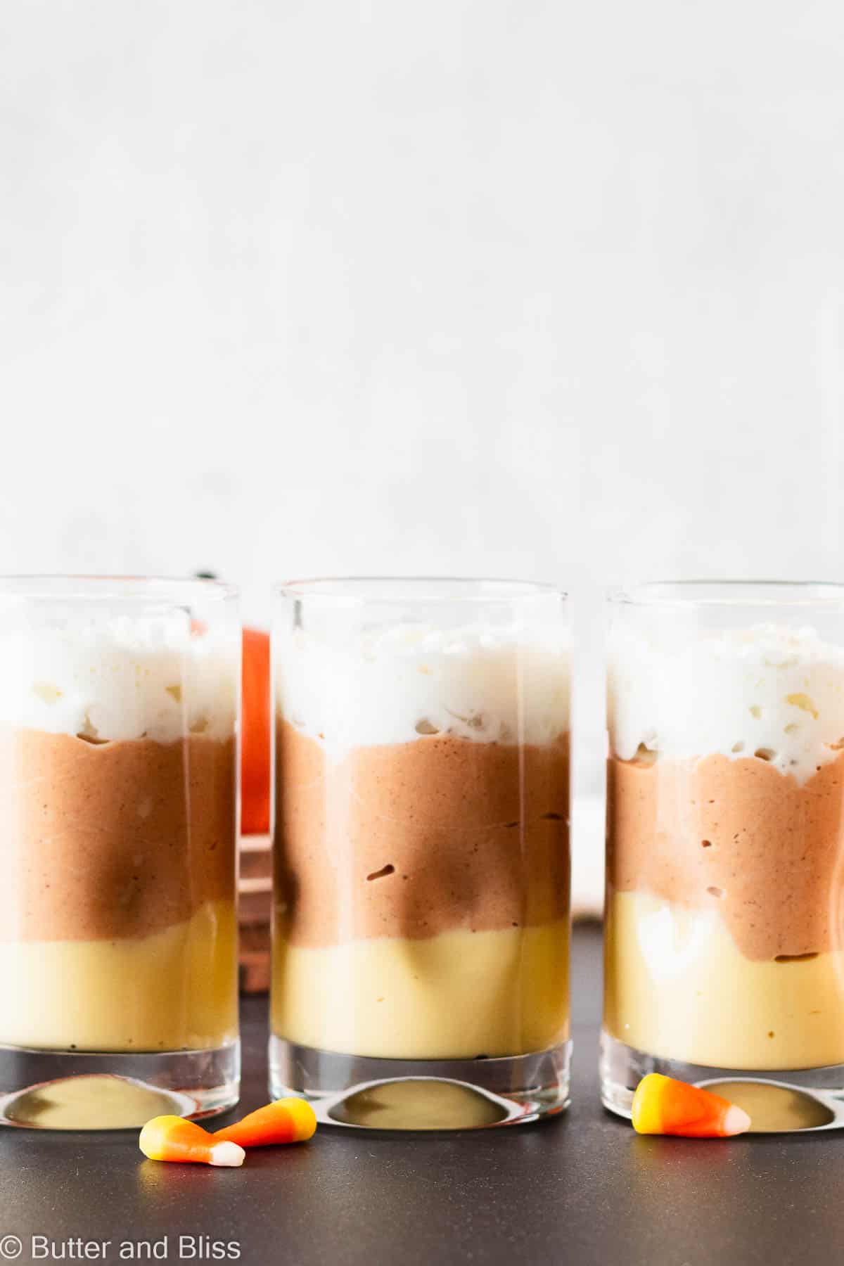Festive halloween candy inspired layered candy corn pudding desserts lined up in a row.