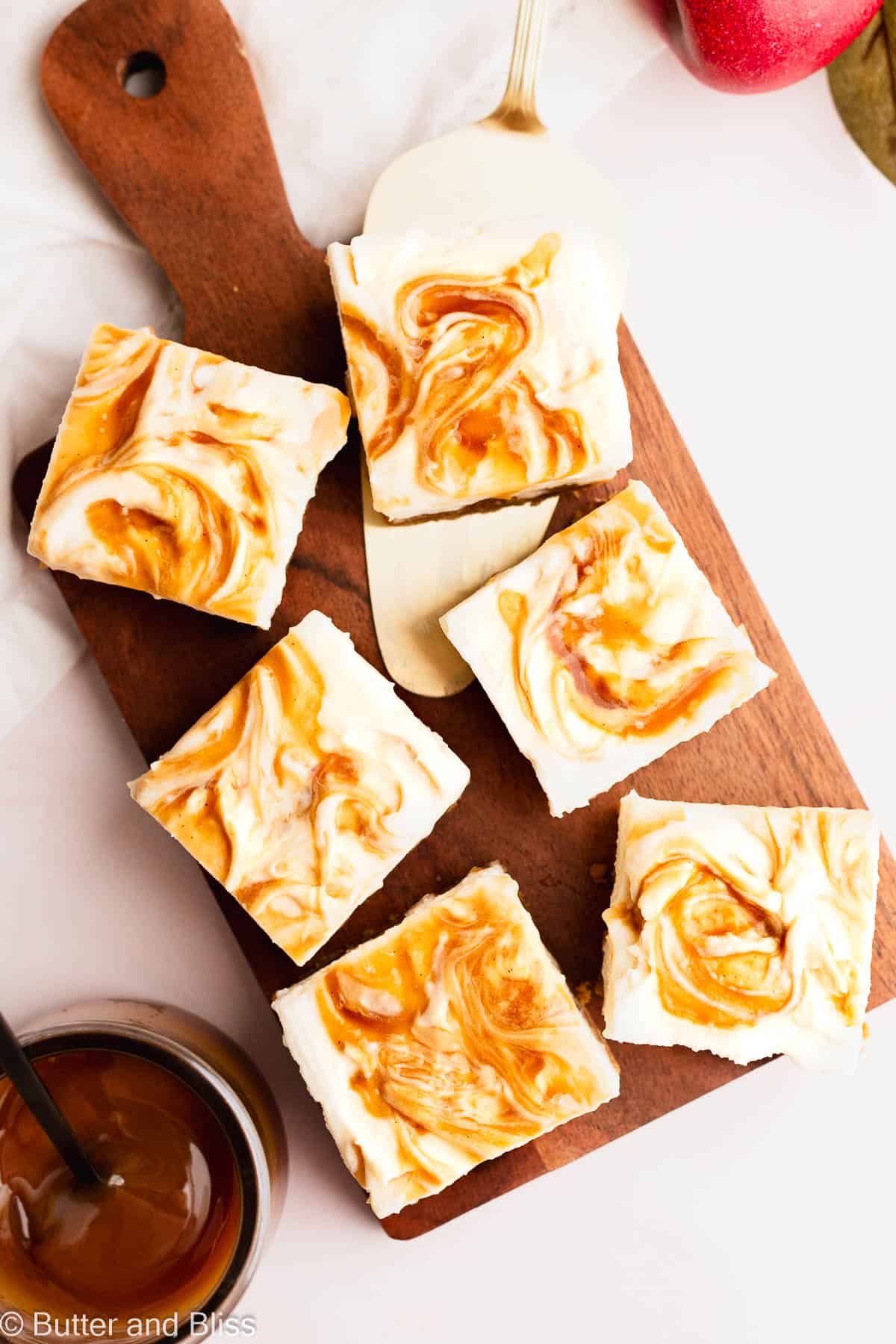 Apple cider cheesecake bars with caramel swirl sliced into perfect squares and arranged on wood cutting board.