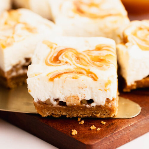 GF apple cider cheesecake bar resting on a cake cutter on a wood cutting board.