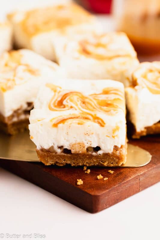 GF apple cider cheesecake bar resting on a cake cutter on a wood cutting board.