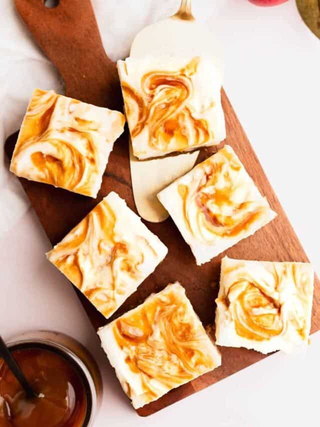 Apple cider cheesecake bars with caramel swirl sliced into perfect squares and arranged on wood cutting board.