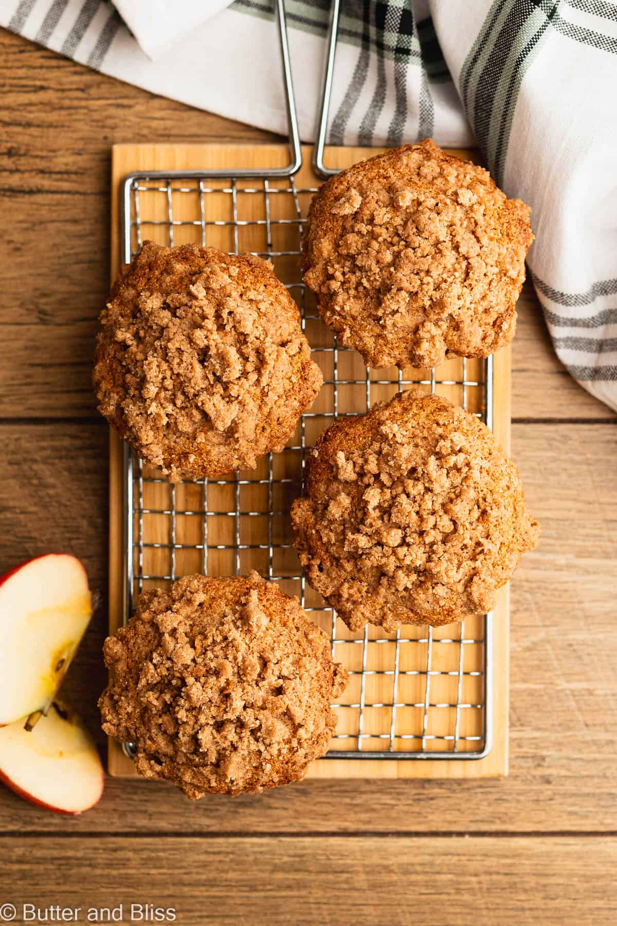 Four apple streusel gluten free muffins on a wire cooling rack on a table.