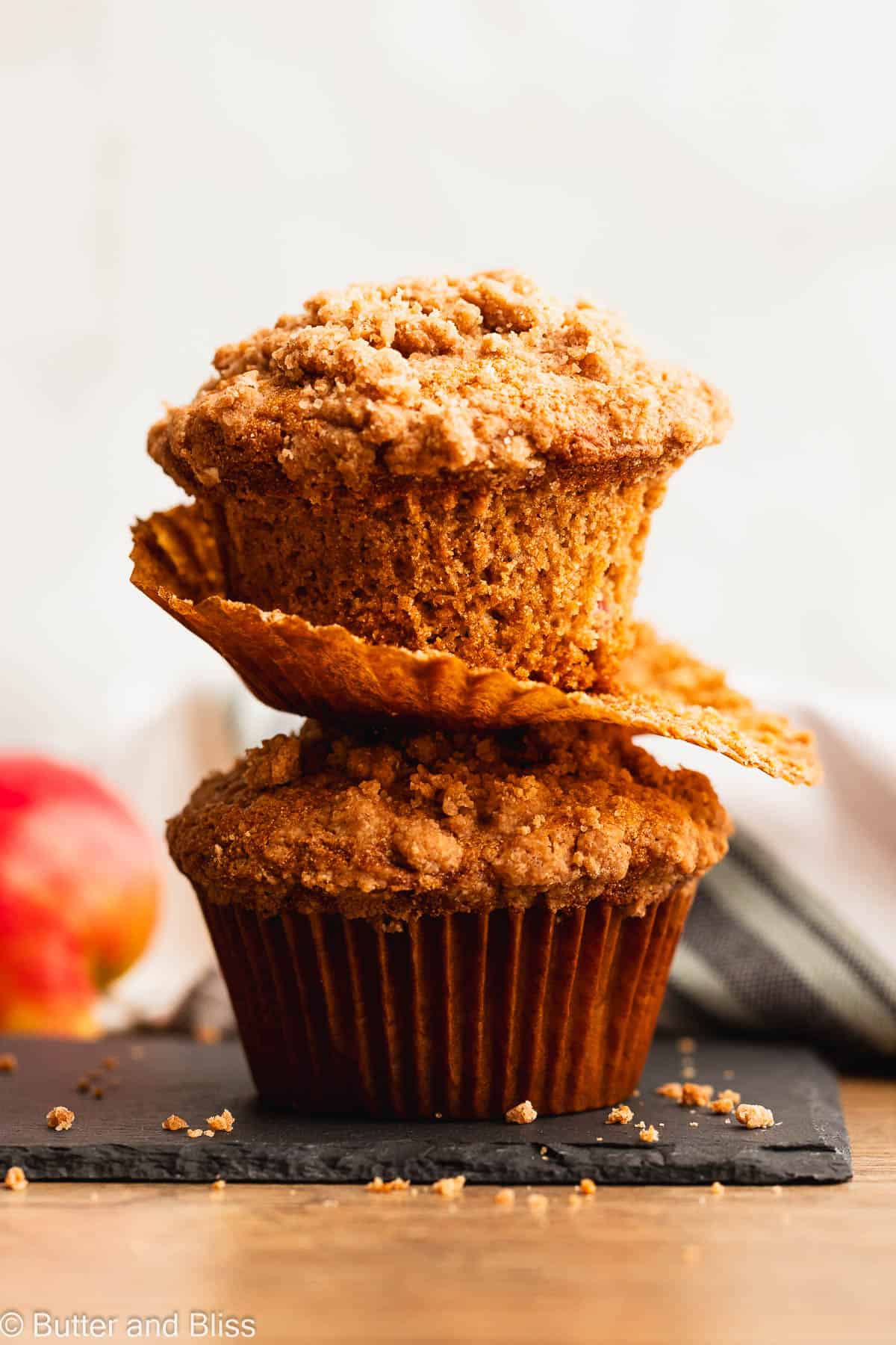 Two apple streusel gluten free muffins stacked and one with the cupcake liner peeled back.