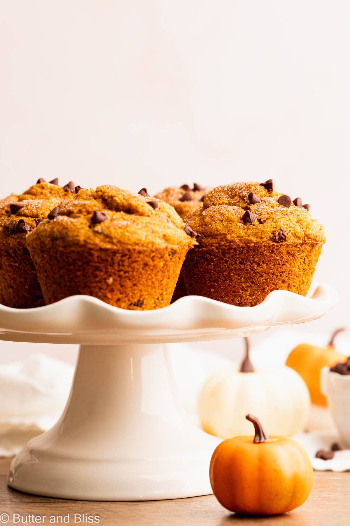 Gluten free pumpkin muffins with chocolate chips arranged on a pretty white cake stand.