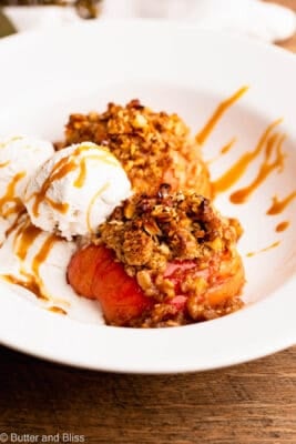 Two halves of fresh baked Hasselback apples in a pretty white bowl and topped with ice cream.