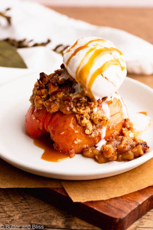 A single serving Hasselback apple on a plate with buttery streusel and topped with ice cream.