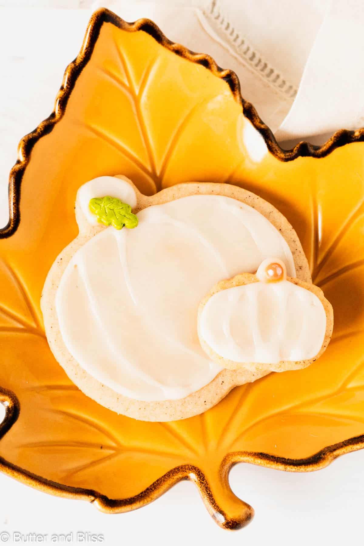 Two cute pumpkin spice cookies in the shape of pumpkins on a fall plate.