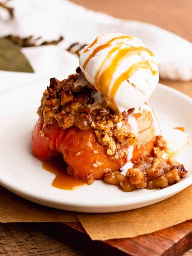 A single serving Hasselback apple on a plate with buttery streusel and topped with ice cream.