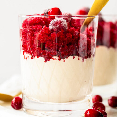 The prettiest glass of holiday granita pudding parfait with a gold spoon and topped with sugared cranberries.
