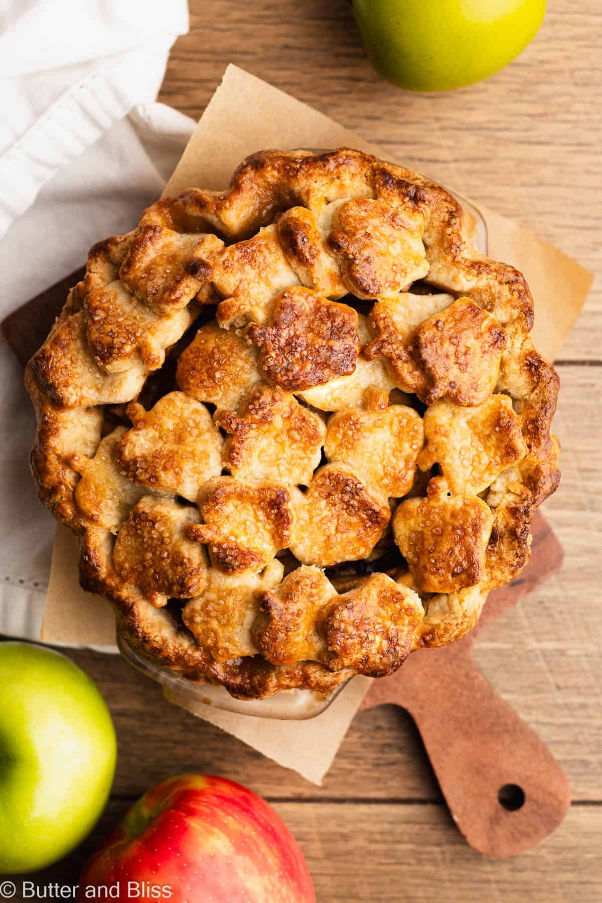 A freshly baked mini gluten free apple pie with apple cut-outs on a wood table.