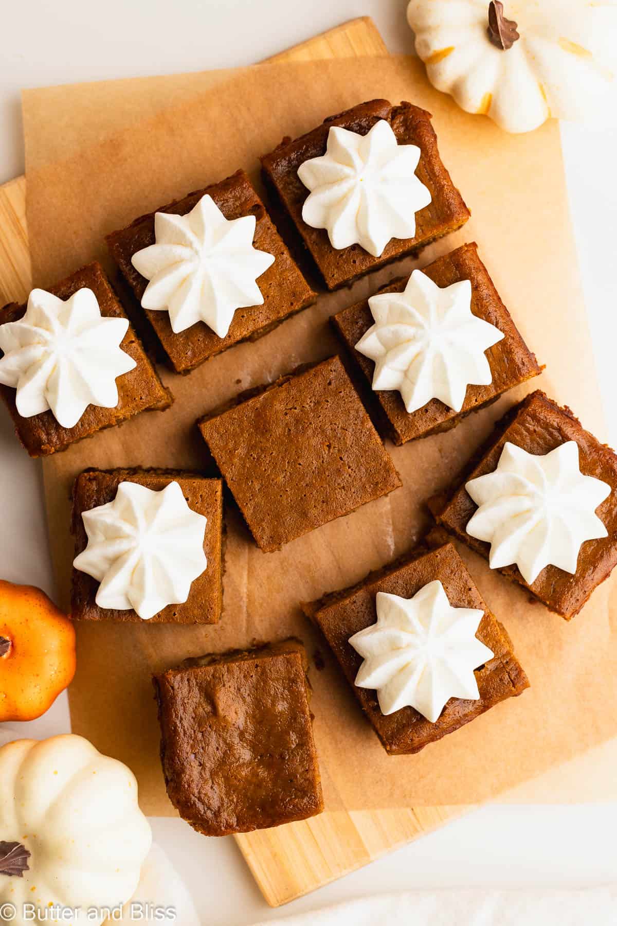 Pretty slices of holiday bars topped with whipped cream set on a piece of parchment paper.