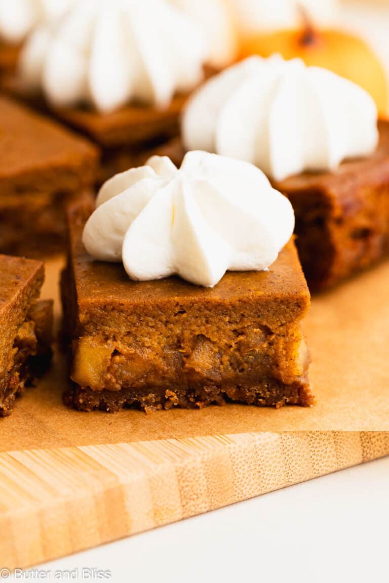 Delicious layers of apple and pumpkin pie in a close up pumpkin pie bar topped with whipped cream.