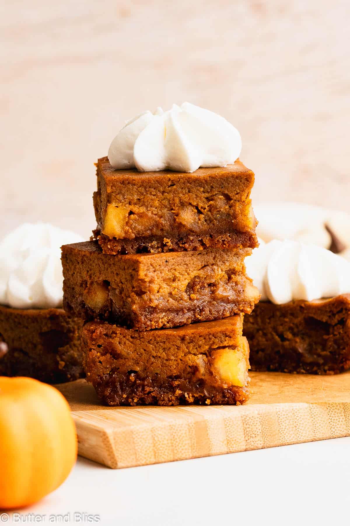 A delicious stack of three gluten free pumpkin apple pie bars on a wood cutting board.