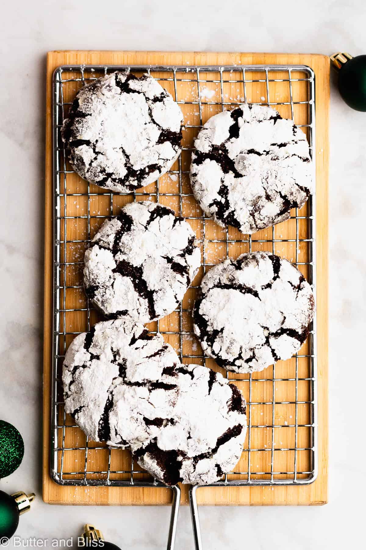 A wire rack with neatly arranged gluten free chocolate crinkle cookies surrounded by green ornaments.