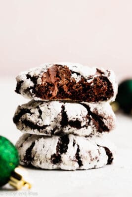 The perfect stack of gluten free chocolate crinkle cookies on a table next to green ornaments.