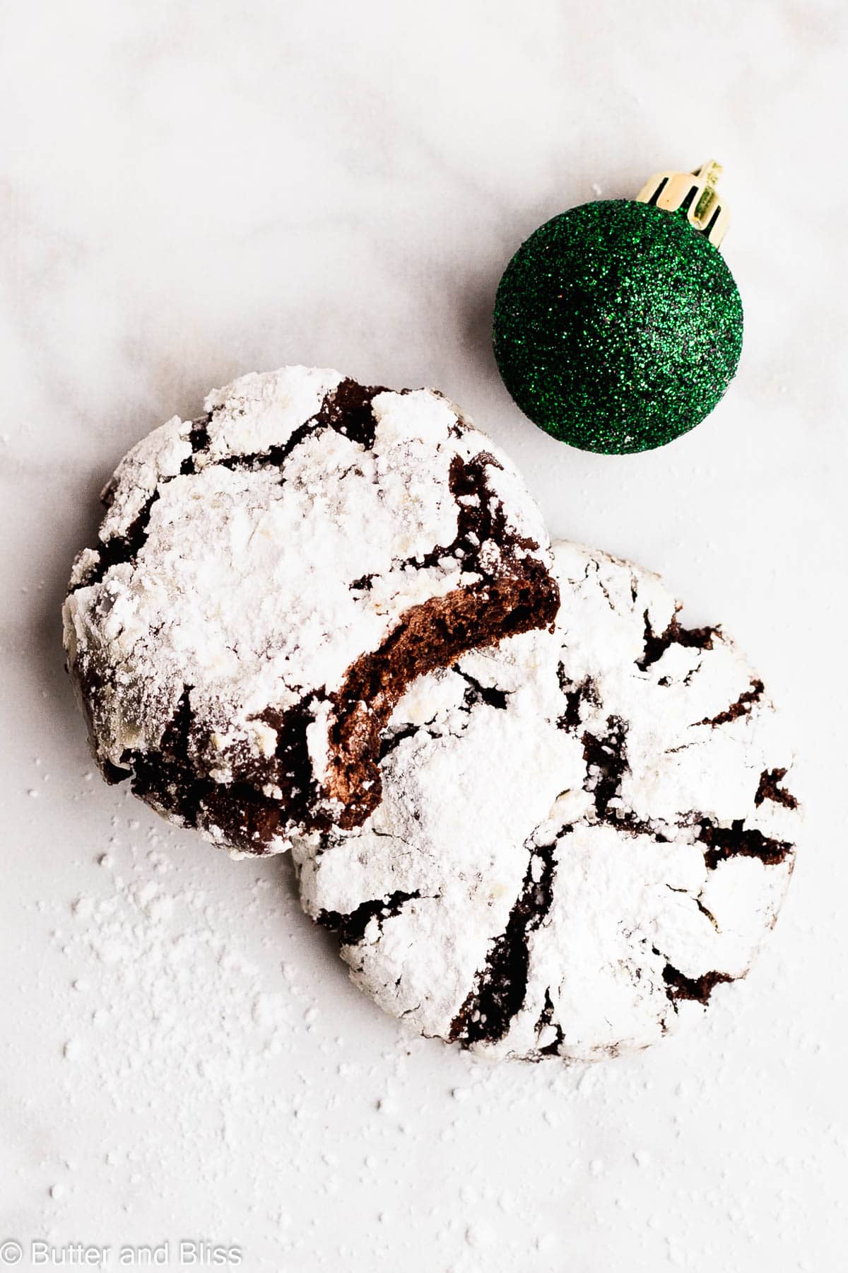 A stack of two festive chocolate crinkle cookies next to a pretty green ornament.