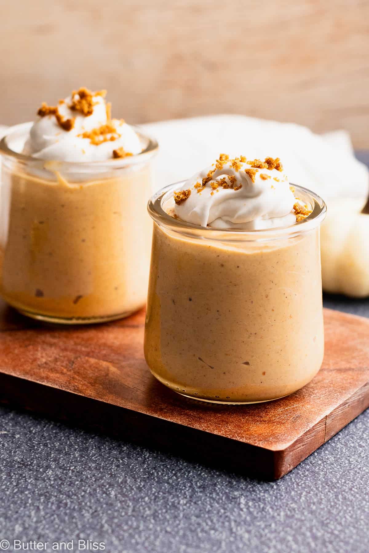 Two pumpkin pudding desserts topped with whipped cream on a wood serving tray.