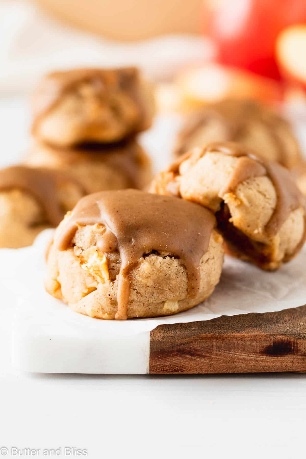 Two super soft apple cookies with caramel icing on a small wood plate.