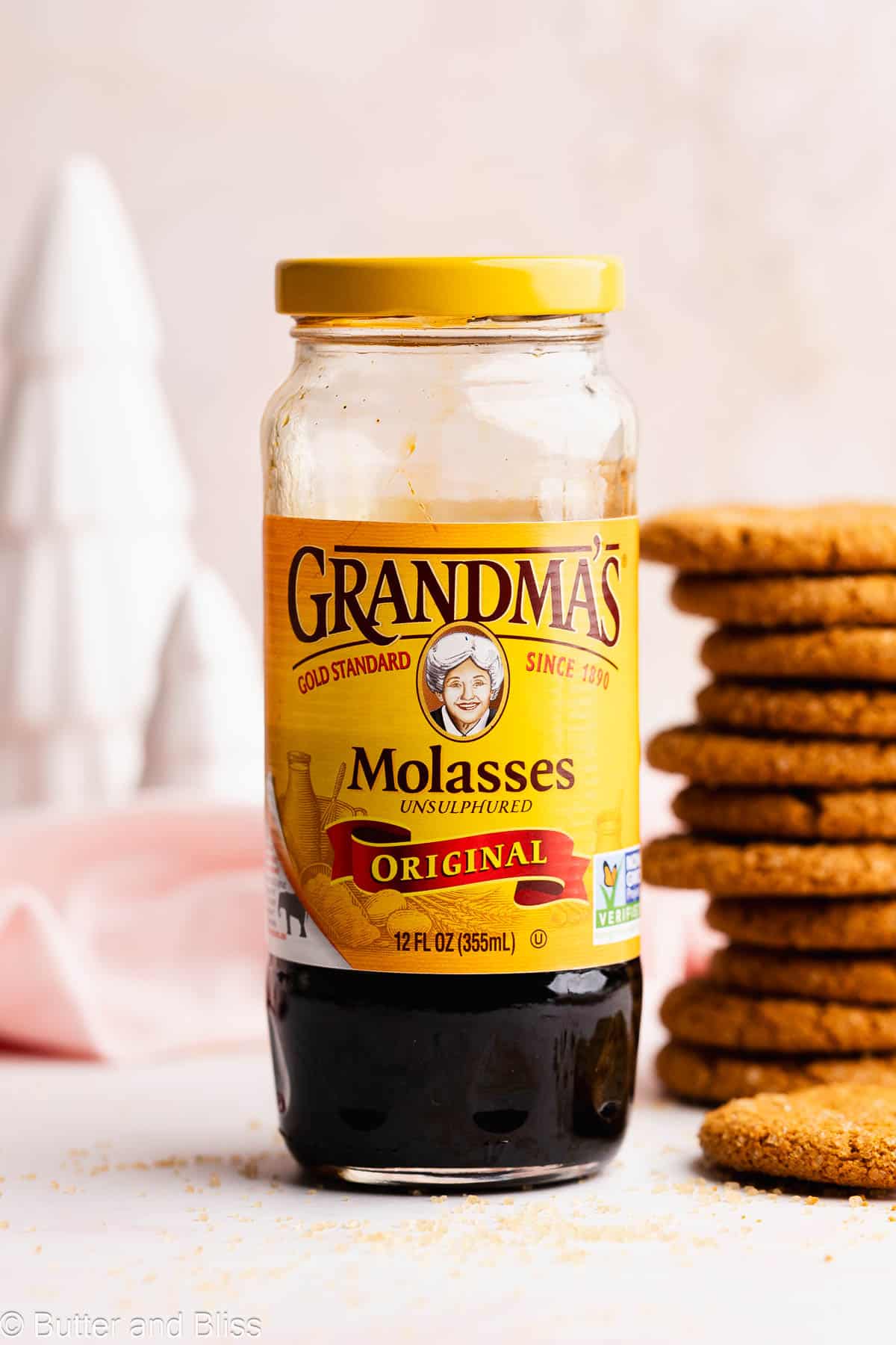 A jar of rich molasses next to a stack of Christmas treats on a white table.