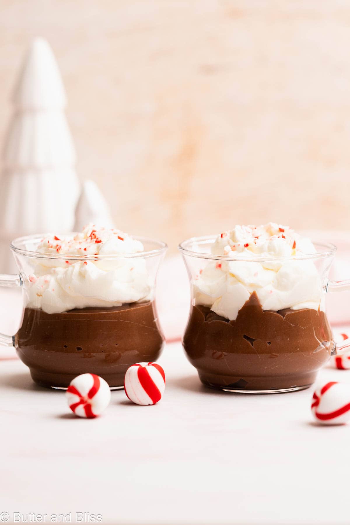 Two clear glasses with hot chocolate pudding topped with marshmallow whipped cream.