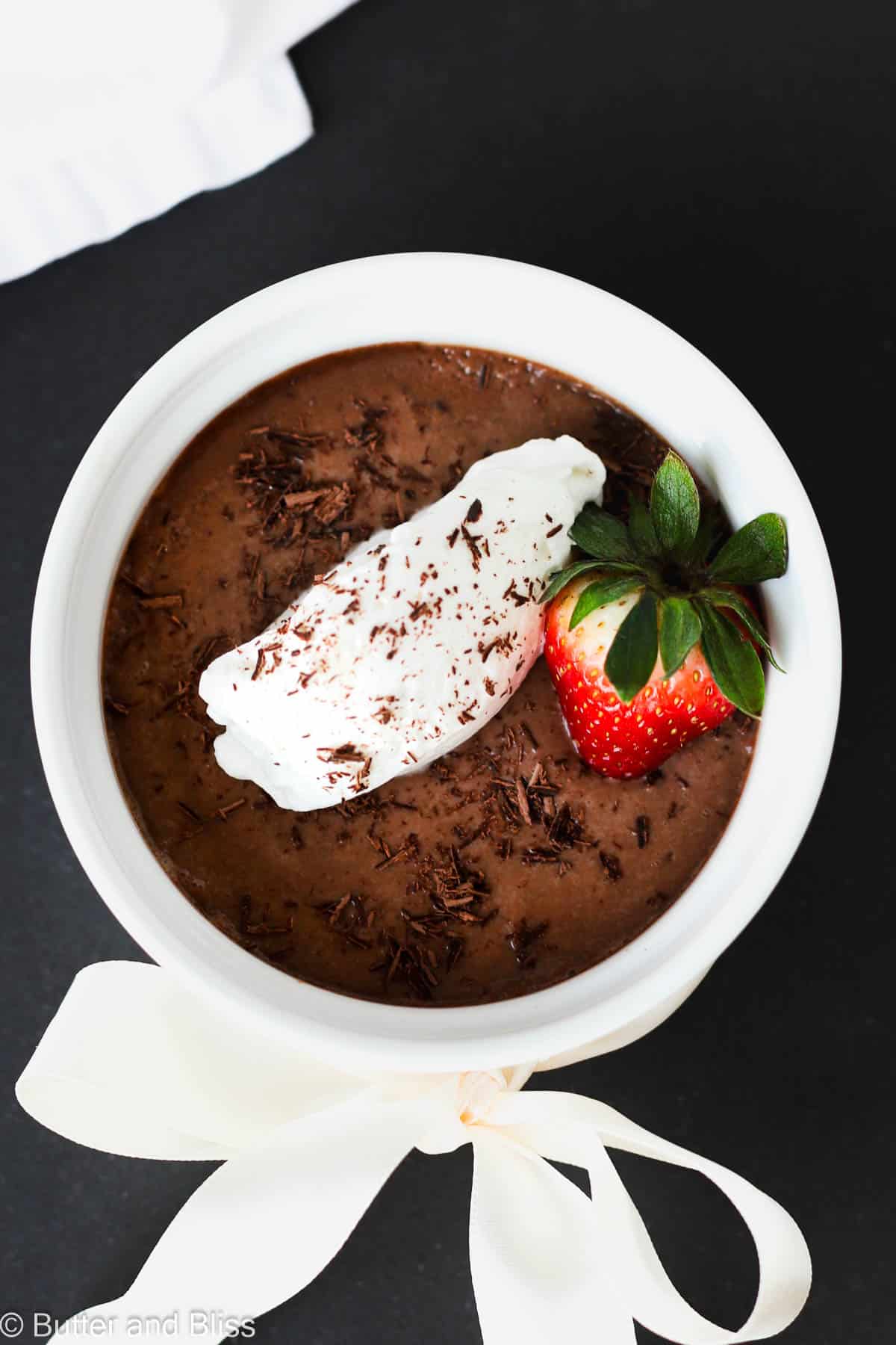 Chocolate pots de creme in a white ramekin with whipped cream and strawberry.