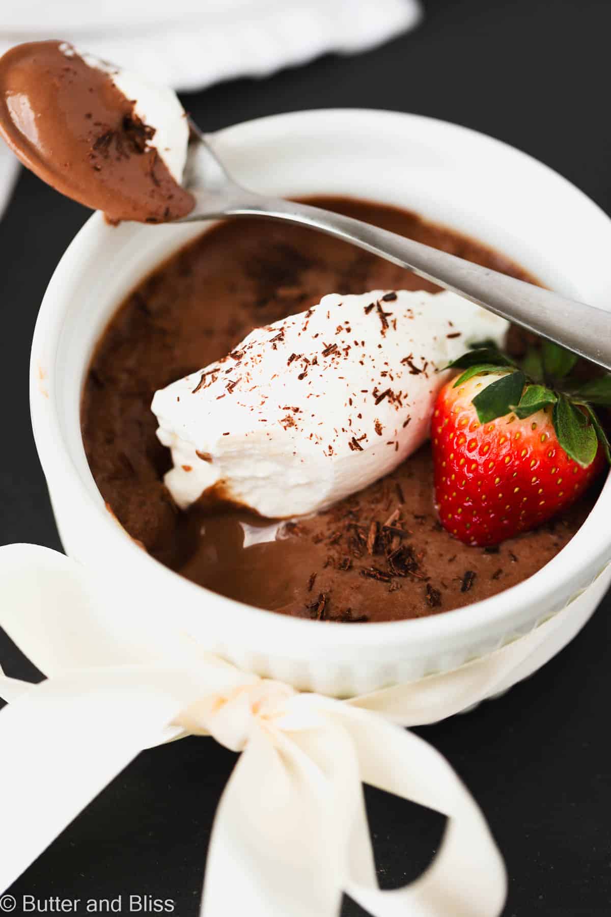Creamy chocolate pots de creme topped with whipped cream in a white bowl.