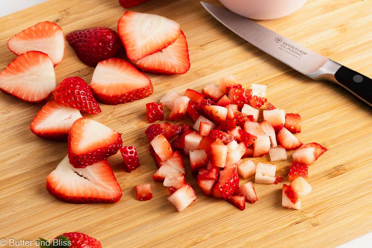 Fresh chopped strawberries on a wood cutting board.