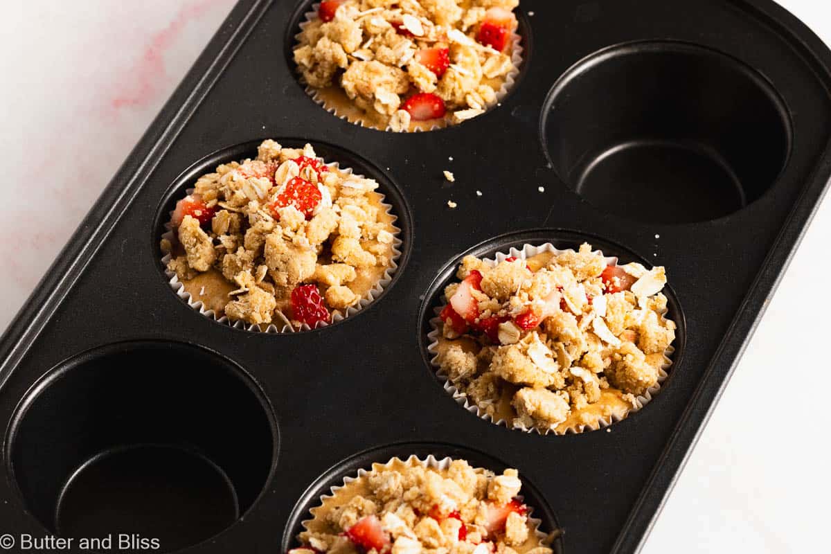 Strawberry muffins topped with oat streusel in a muffin pan waiting to be baked.