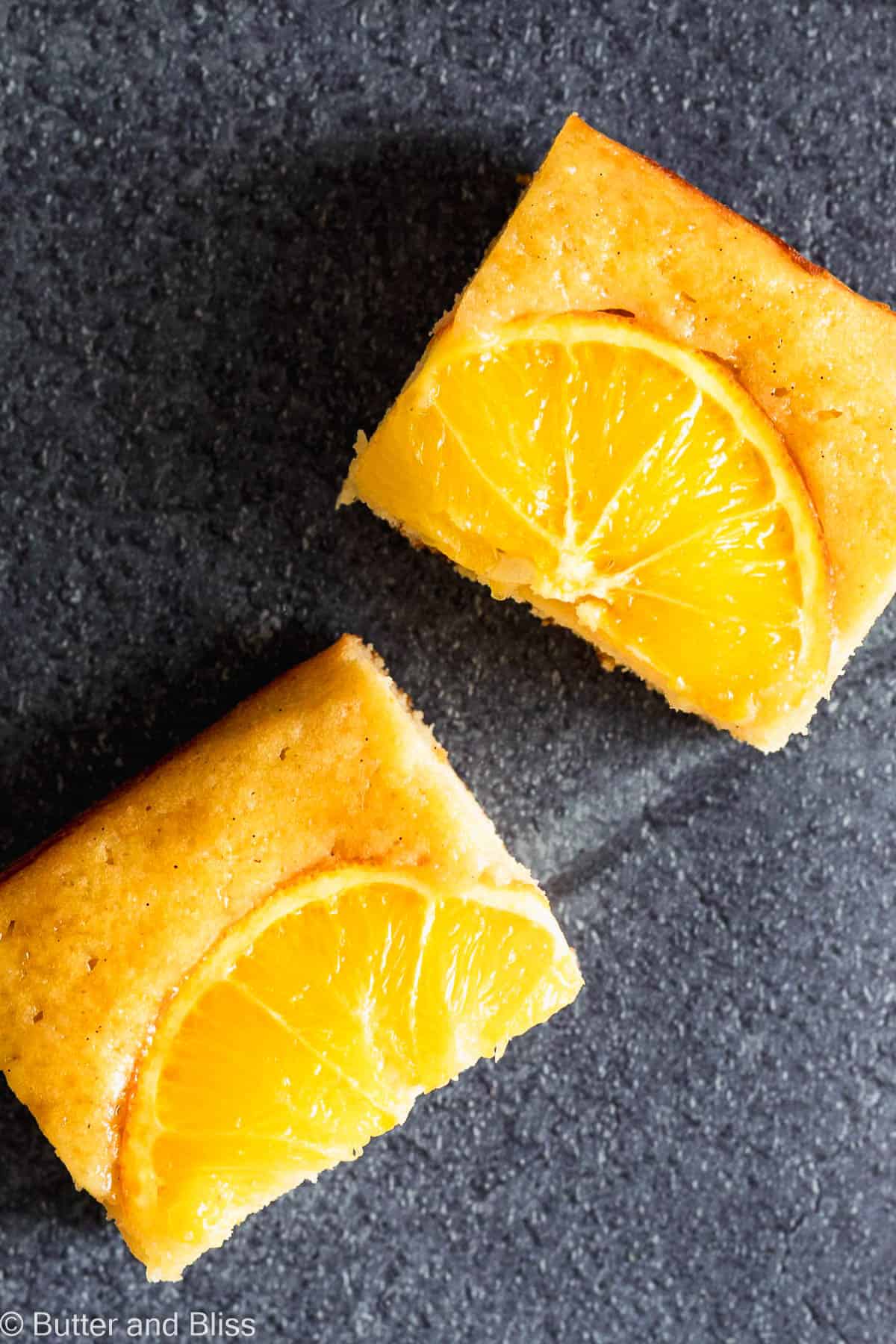 Two pretty slices of orange snack cake with orange slices on a table.
