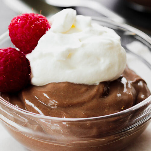 Small batch chocolate pudding topped with whipped cream in small serving bowl.