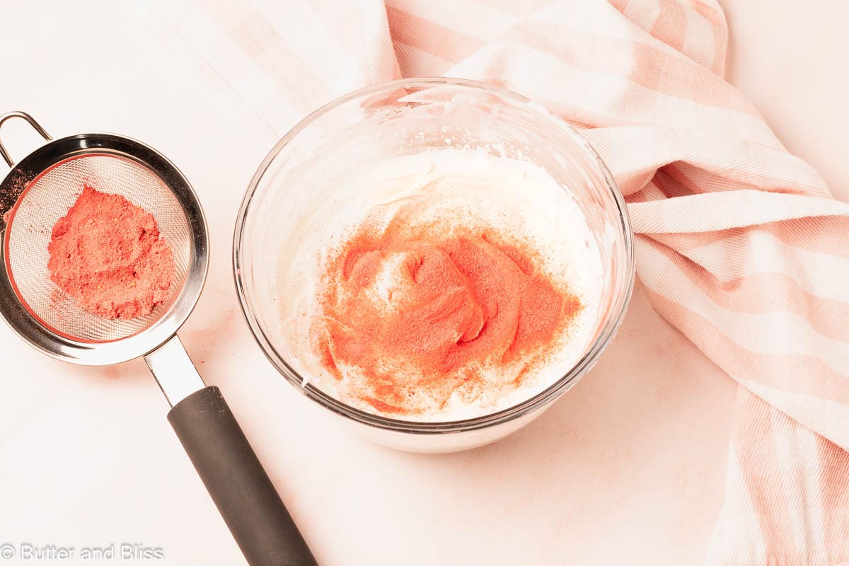 Whipped cream in a glass bowl with strawberry powder sprinkled on top.