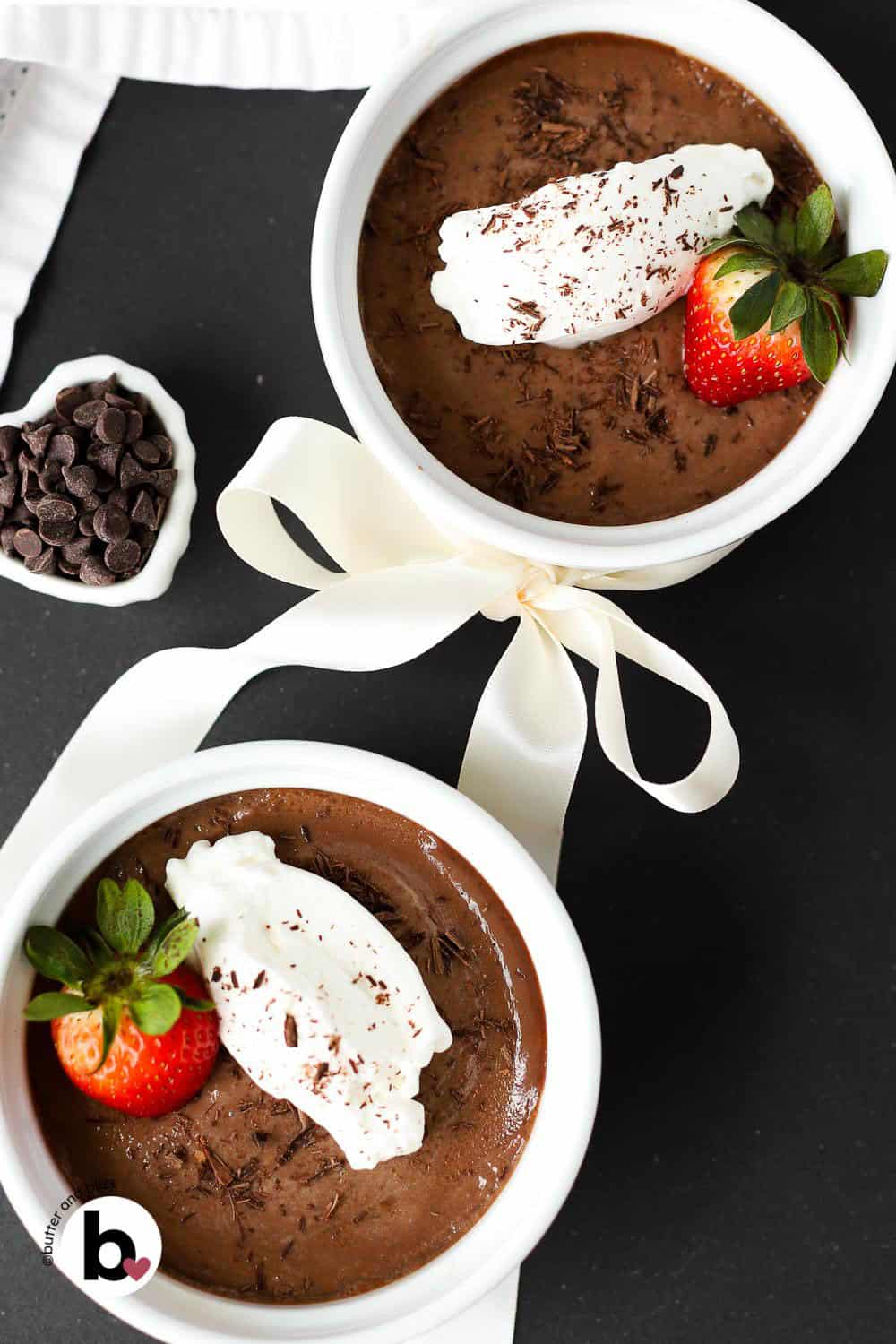 Two chocolate pots de creme in small ramekins with a heart bow around the bowls.