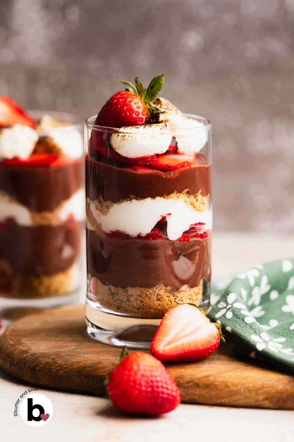 Chocolate s'mores parfaits in two glasses, with layers of pudding, strawberries, and marshmallow.