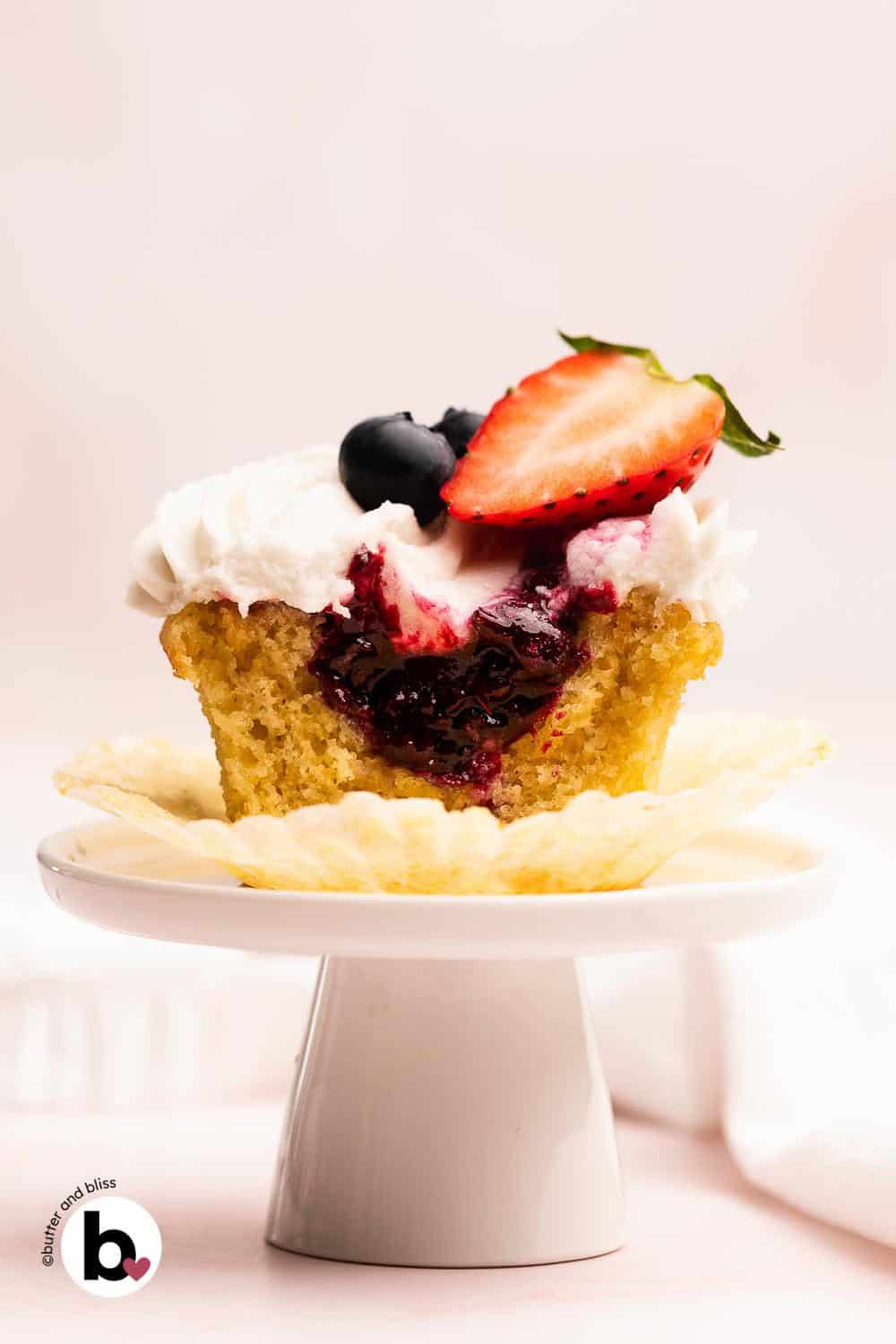 Single vanilla cupcake with berry filling sliced open on a small cupcake stand.