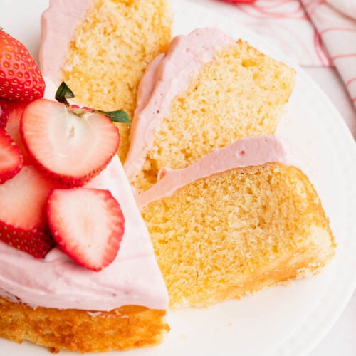 Pretty slices of a small vanilla cake topped with strawberry frosting fanned out on a plate.