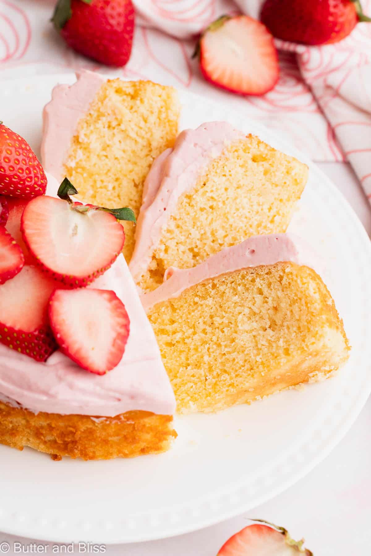 Pretty slices of a small vanilla cake topped with strawberry frosting fanned out on a plate.