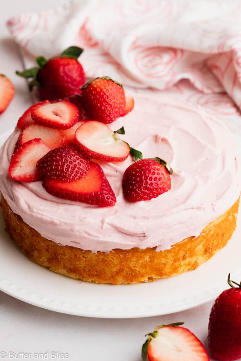 A small strawberry frosted vanilla cake on a white plate.