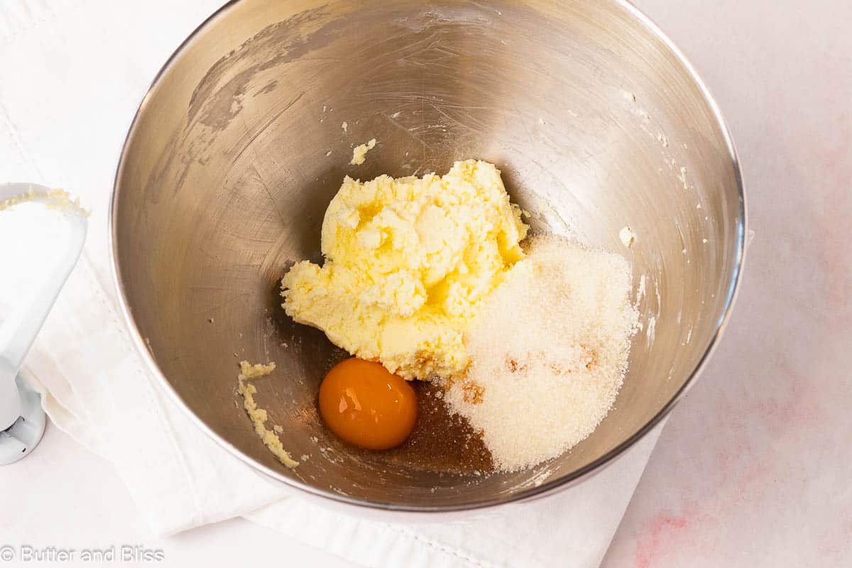 Egg and sugar added to whipped butter in a mixing bowl.