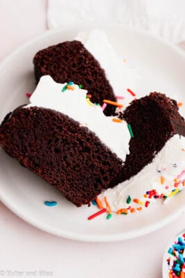 Slices of chocoalte wacky cake with whipped cream frosting on a white plate.