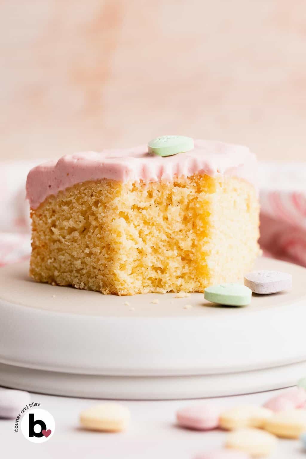 A slice of vanilla cake on a white plate with heart candies.