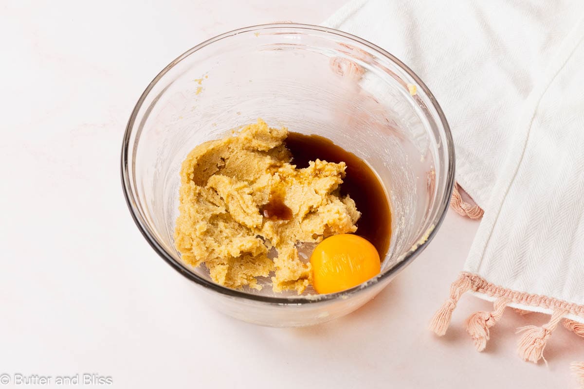 Egg yolk added to creamed butter and sugar in a mixing bowl.