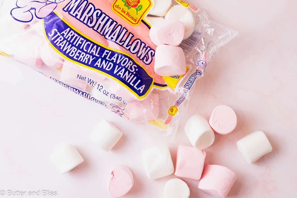 Strawberry and vanilla jumbo marshmallows spilling out of the bag on a table.