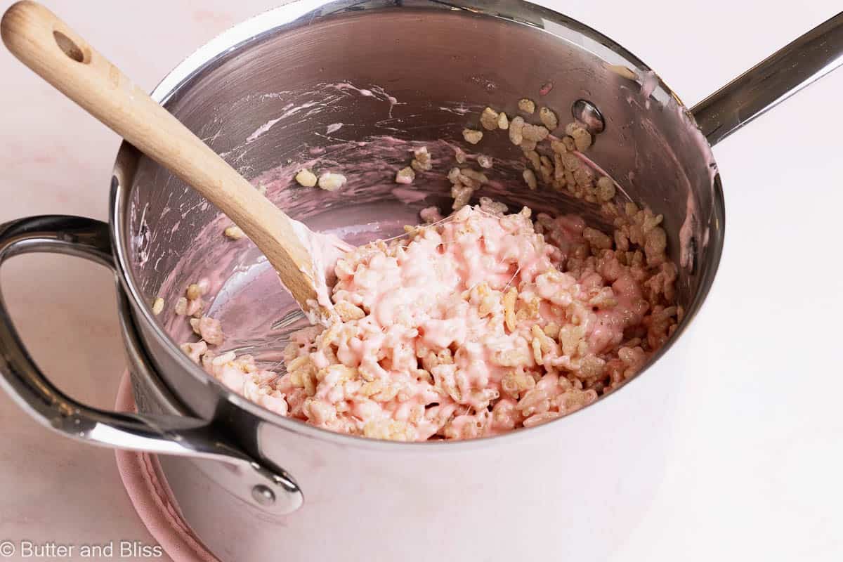 Strawberries and cream rice krispies being mixed in a large saucepan.