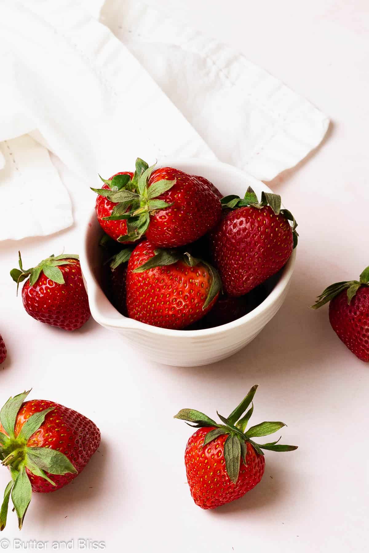 Fresh strawberries spilling out of a small white bowl.