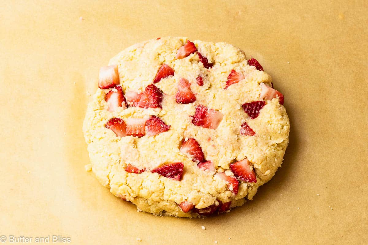 Scone dough dotted with fresh strawberries on a baking sheet.