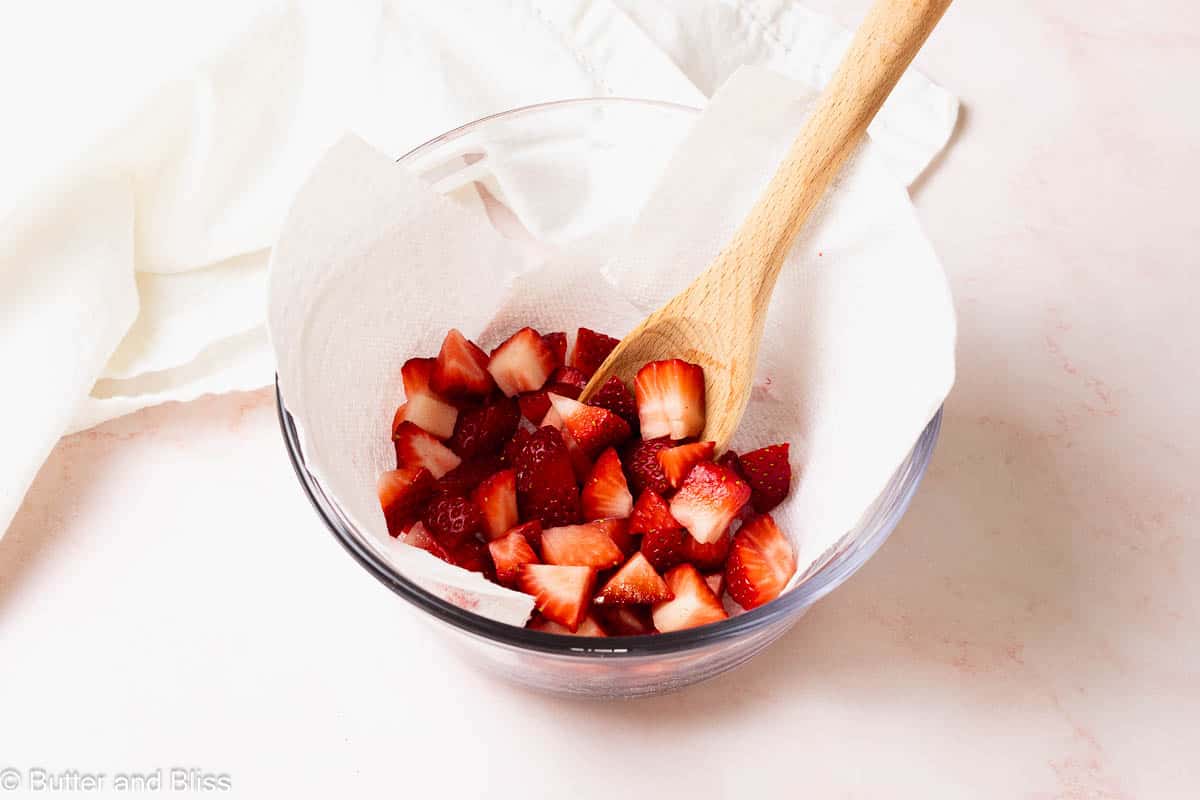 A paper towel lined bowl of freshly chopped strawberries.