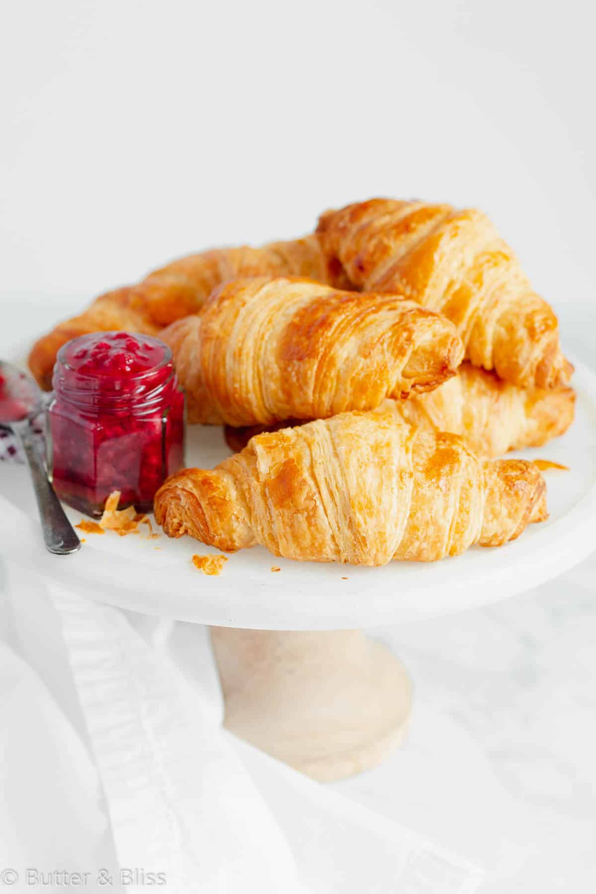 A white serving platter full of buttery homemade croissants with side of jam.