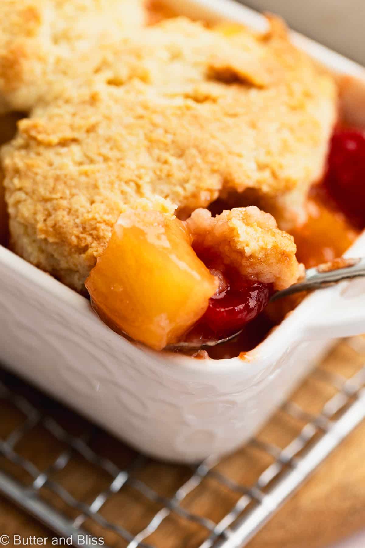 Gooey chunk of pineapple and cherry on a spoon in a pineapple upside down cobbler.